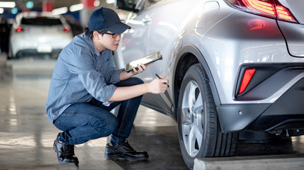 Canvas Print - Young Asian auto mechanic holding digital tablet checking car wheel in auto service garage. Mechanical maintenance engineer working in automotive industry. Automobile servicing and repair concept