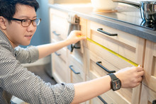 Young Asian Man Using Tape Measure For Measuring Drawer On Wooden Kitchen Counter In Showroom. Shopping Furniture For Home Improvement. Interior Design Concept
