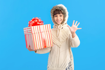 Wall Mural - Little girl in winter clothes with a big gift box in hands on a blue background. Show five fingers. Christmas holiday gifts.