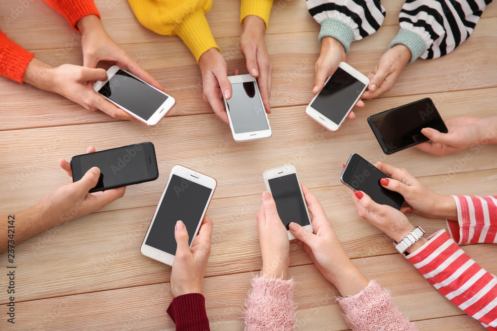 Young people using mobile phones at wooden table. Concept of addiction