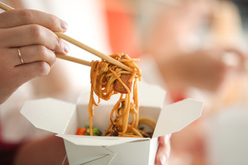 woman eating chinese noodles from takeaway box, closeup