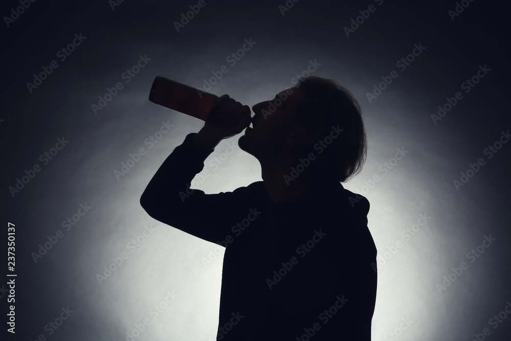 Silhouette of man drinking beer on dark background. Alcoholism concept