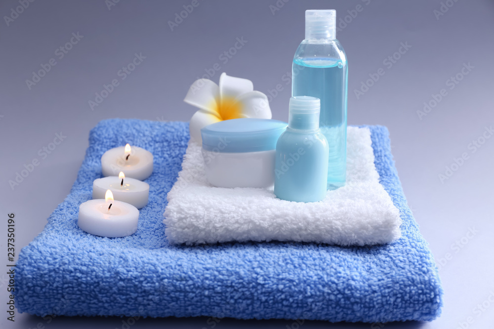 Spa composition with burning candles, towels and cosmetics on color background