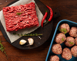 Wall Mural - Minced beef meat and meatballs with salt, garlic, herbs on wooden table. Top view.