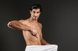 © Drobot Dean - Young man posing isolated over dark wall background holding razor covering his genitals with towel.