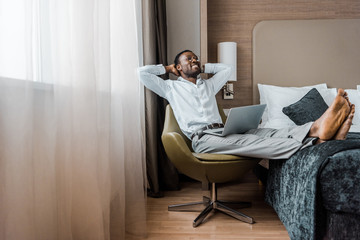 smiling young african american businessman relaxing in hotel room with laptop