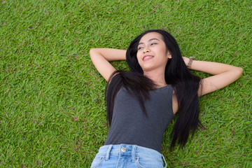 Happy young beautiful Asian woman laying down on grass at the park