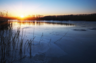  Winter landscape with frozen river, reeds and sunset sky. Daybreak