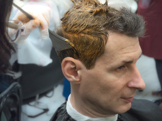 The process of hair coloring on a man in a beauty salon. Close up.