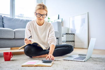 Young woman counting bills and managing home finances with notebook and laptop