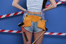 Short Girl Shorts In Pockets Which Construction Tools On Blue Background. Gloves, Screwdriver And Hammer