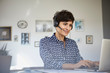© Westend61 - Smiling woman at home with headset using laptop