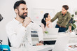 © LIGHTFIELD STUDIOS - thoughtful office manager sitting in office with coworkers on background