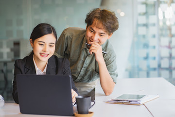 Smiling attractive asian woman talking to male colleague at work sharing office desk with laptops