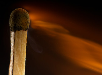 Burning wooden match with a red match head on a black background.