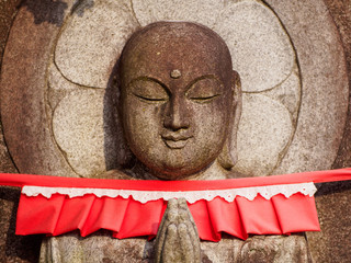 closeup of a bosatsu, stone buddha statue, praying with traditional red cloth bib. kyoto, japan. tra