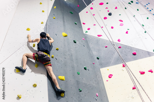Cuadros en Lienzo Rear view of man climbing wall with help of grip