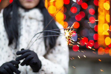 Closeup shot of brunette woman having fun with sparklers at the garlands blurred background. Space for text