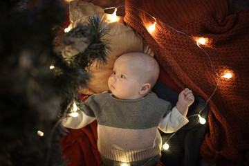 Baby in a sweater next to Christmas tree, festive