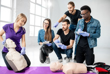 Group Of Young People Learning To Make Artificial Breathing With Medical Dummies During The First Aid Training In The White Room