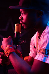 Wall Mural - Studio portrait of young man with beard and mustaches in baseball cap and t-shirt with microphone. Pink neon light