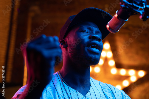 Cuadros en Lienzo Man with beard and mustaches in baseball cap and t-shirt sing in microphone