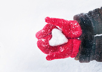 Female hands in knitted mittens with heart of snow in winter day. Love concept. Valentine day background.