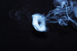 White smoke ring on black fabric background. Smoke spreads over the background. Vaping culture, life without cigarettes. Conceptual image.