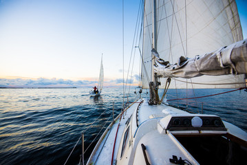 Clear evening sky at sunset. Two yachts sailing. A view from the deck to the bow and sails, close-up. Baltic sea, Latvia