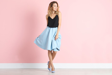 Young woman with beautiful long legs in stylish outfit near color wall