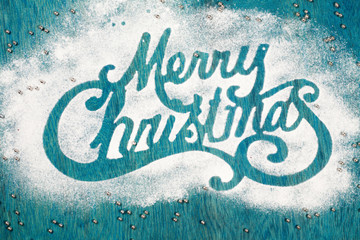 Wall Mural - Merry Christmas sigh made out of sugar powder on blue background, flat lay