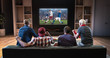© haizon - Group of fans are watching a soccer moment on the TV and celebrating a goal, sitting on the couch in the living room.