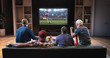 © haizon - Group of fans are watching a soccer moment on the TV and celebrating a goal, sitting on the couch in the living room.