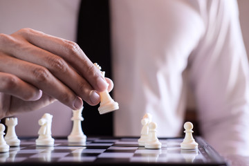 Wall Mural - Hand of confident businessman use king chess piece white playing chess game to development analysis new strategy plan, business strategy for win and success
