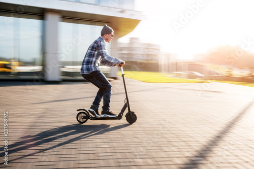 Fotografía Young man in casual wear on electric kick scooter on city street in motion blur
