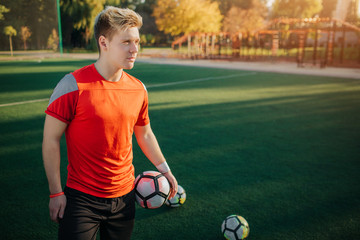 Wall Mural - Nice and good-looking athlete stand with ball in hands. Guy is on lawn. He looks forward. Weather is sunny.