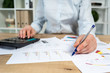 © brizmaker - Cropped close up photo of lady in her formalwear she sit behind table with charts graph diagram in bright loft interior mark important spot on graphics by pen focus on hand