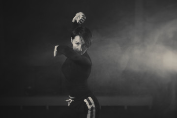 modern beautiful dancer in black clothes posing against the Studio in the smoke