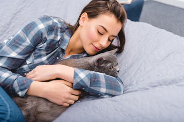 Wall Mural - high angle view of happy girl lying on bed with british shorthair cat