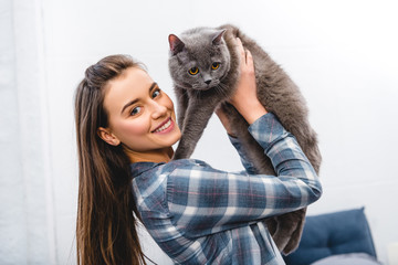 Wall Mural - happy young woman holding british shorthair cat and smiling at camera