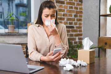 Wall Mural - young businesswoman using smartphone and suffering from allergy at workplace