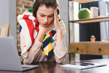 sick young businesswoman in scarf suffering from headache at workplace