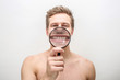 © estradaanton - Happy young man showing his teeth through magnifying glass. He looks straight. Isolated on white background.