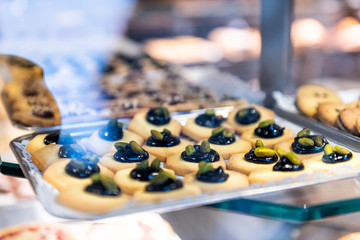 Shortbread Italian style cookies on retail display in store, shop, bakery through window, with whole pistachio and black caramel on top on tray