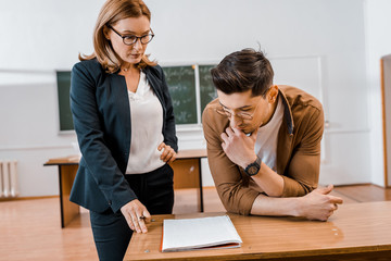 serious female teacher and male student during exam in classroom