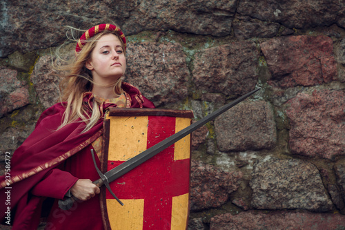 Foto a brave young girl in a Burgundy Cape with a shield and a sword stands near the