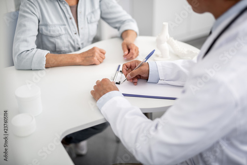 Fotografía Careful attentive doctor making necessary notes on the clipboard and his patient