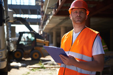 Professional Foreman In Building Uniform Standing And Holding Blue Clipboard While Looking Into The Distance