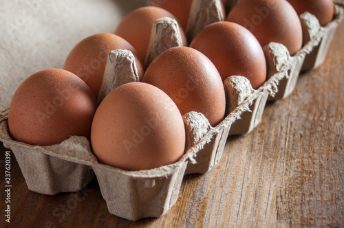 Large brown chicken eggs in green carton packaging on wooden table.