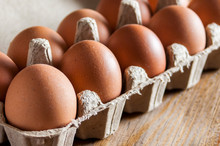 Brown Chicken Eggs In Carton Packaging On Wooden Table.